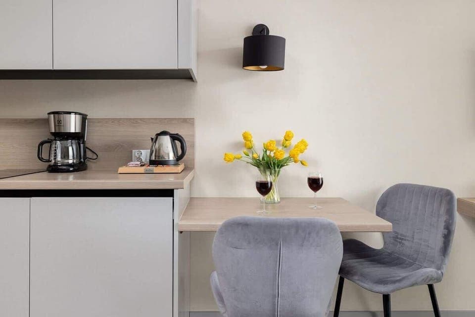 Compact kitchenette with coffee maker, dining area, and yellow floral accents.
