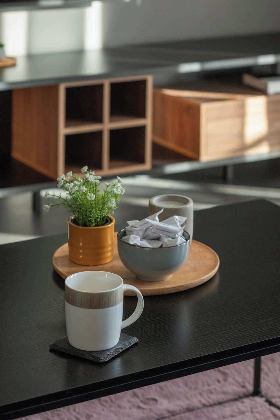 Close-up of a coffee table on which stands a decorative tray with a flower. A cup stands next to it. 