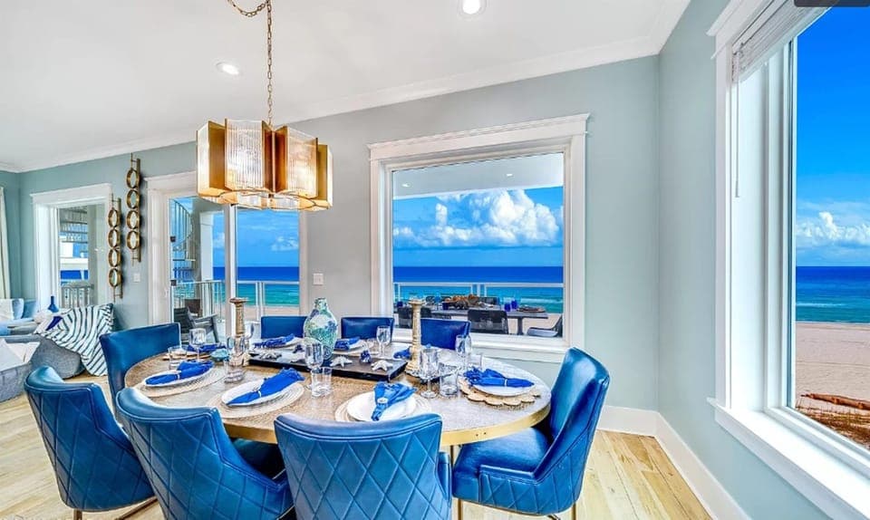 Savor memorable meals with stunning ocean views through expansive windows, where elegant blue chairs create a sophisticated coastal dining experience.