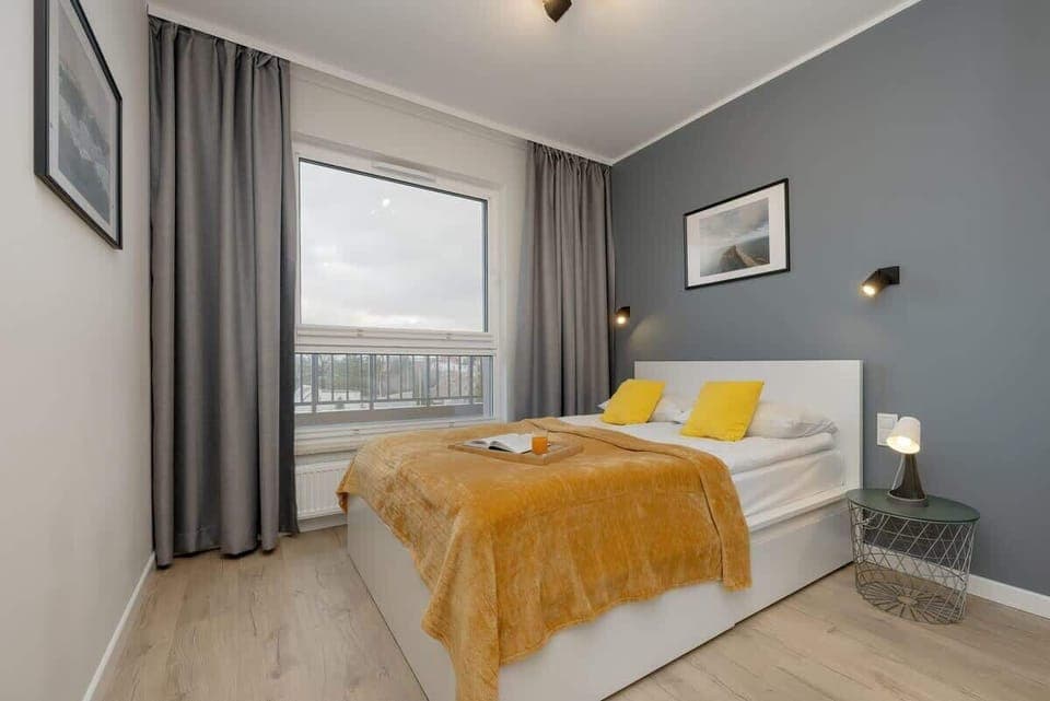 Bedroom with a double bed, gray accent wall, large windows, and a yellow blanket adding a pop of color.