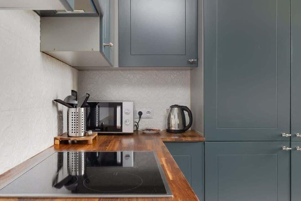 A kitchen corner with navy-blue cabinetry, a wooden countertop, and modern appliances, offering a functional and stylish cooking space.

