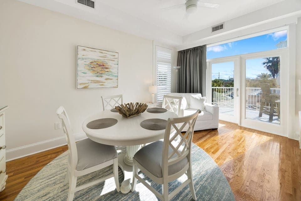 Gather around your elegant dining table where coastal charm meets comfort. Sunlight streams through French doors leading to your private balcony retreat.