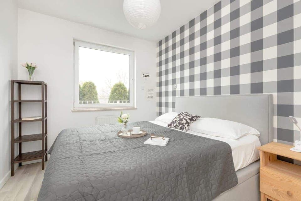 Cozy bedroom with a double bed, wooden side table, and a stylish black-and-white checkered accent wall.