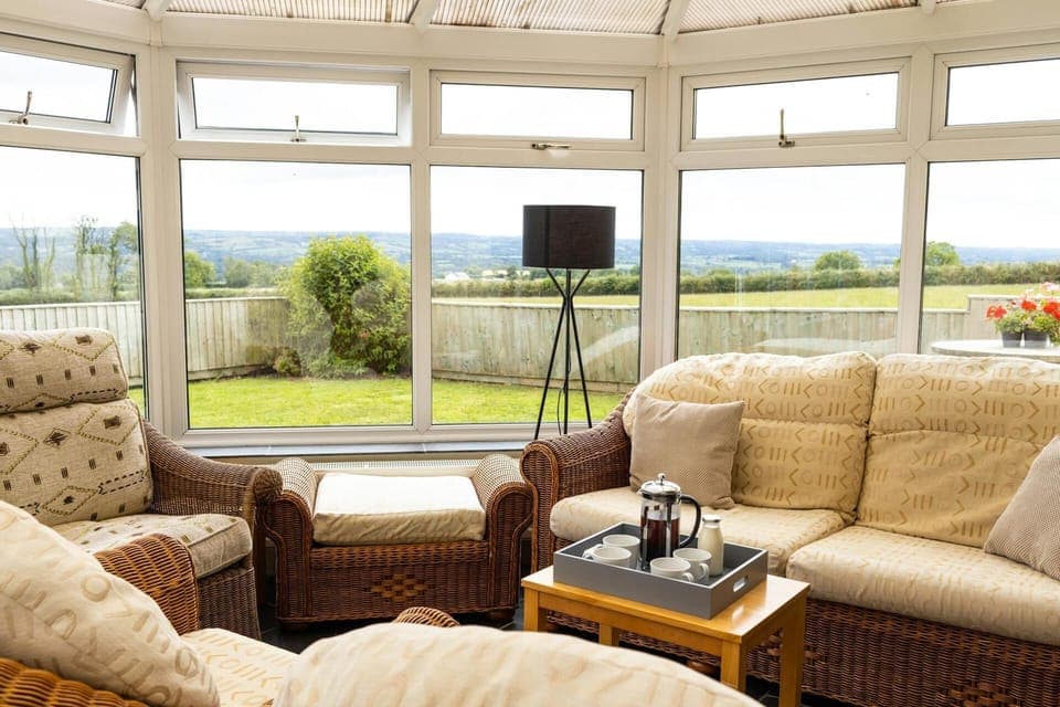 Conservatory with sofas and a small table with views out to the hills