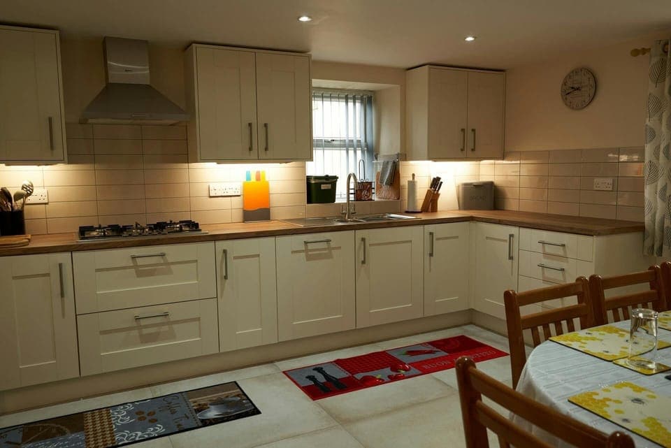 Kitchen cabinets, under cabinet lighting, hob, sink, dining table and chairs