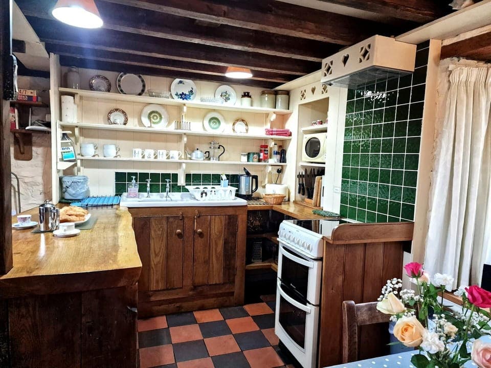 Kitchen with electric cooker, sink, shelving with crockery, kettle, microwave and toaster