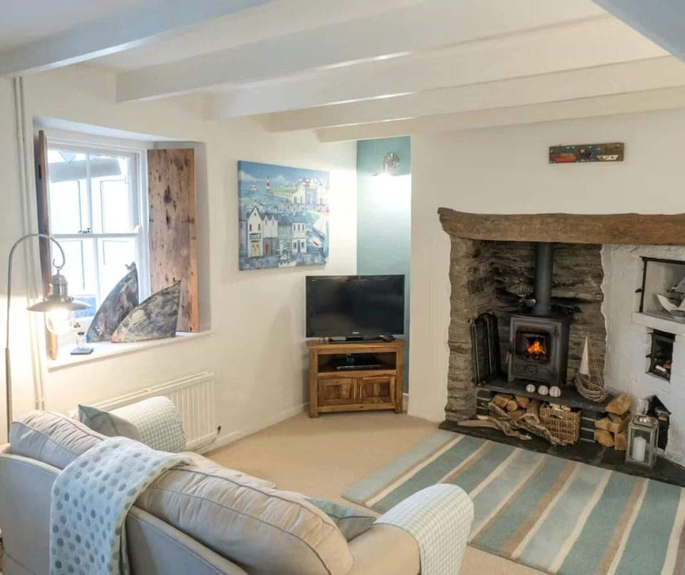 Living room with sofa, window with driftwood shutter, fireplace with woodburner