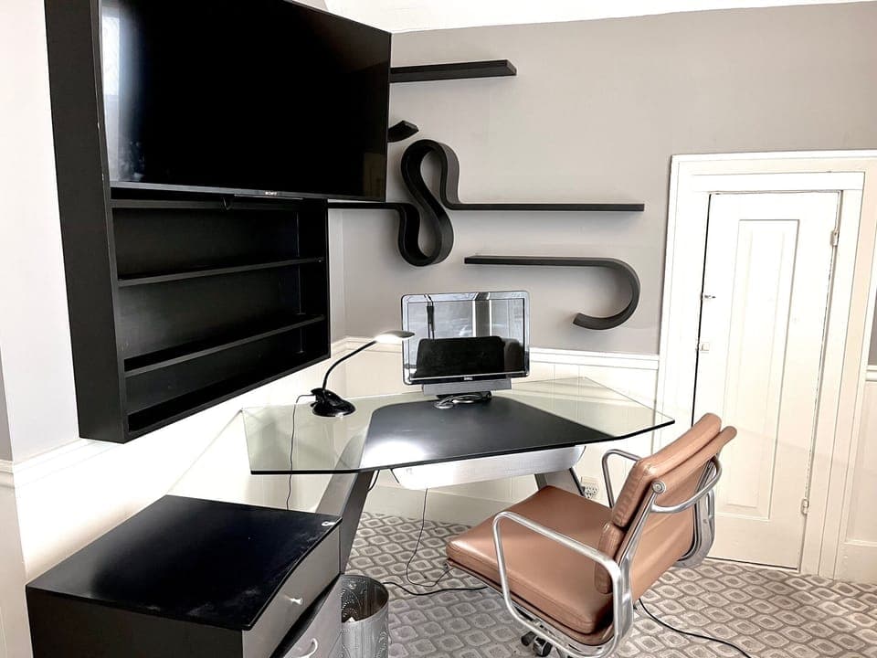 Glass desk, leather chair and TV extended from bookcase (monitor for scale only)