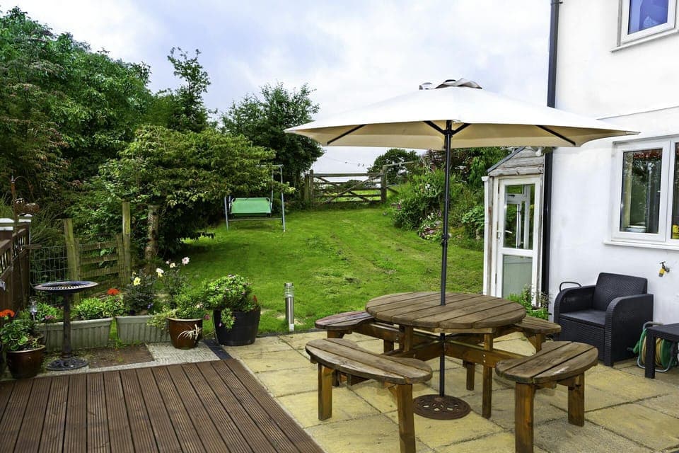 Patio area with table, seating, parasol. lawned garden and flowers