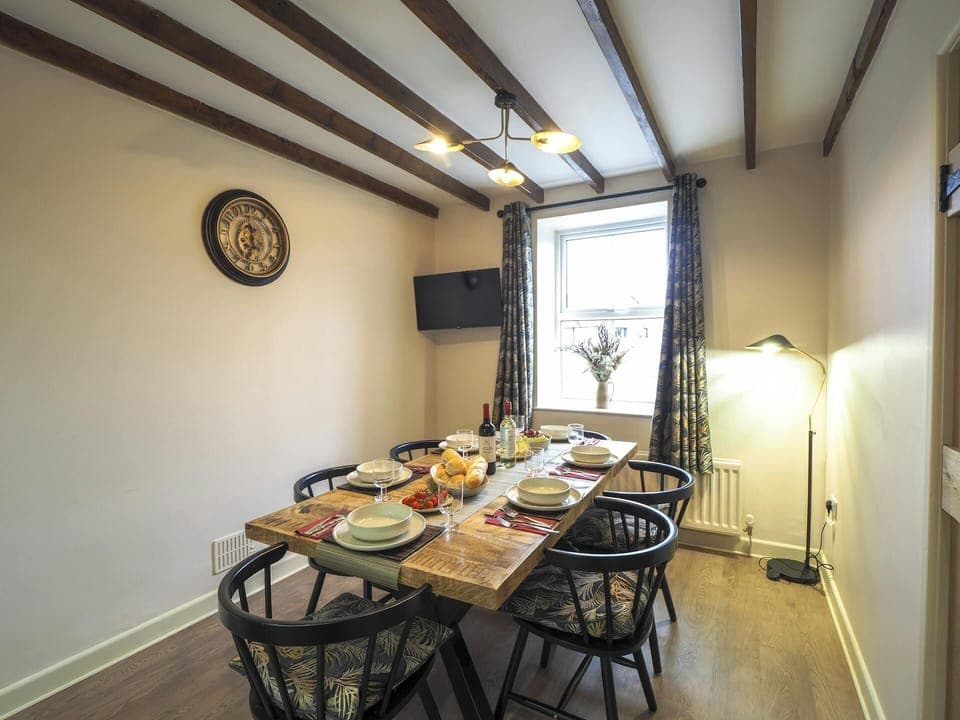 Table and six chairs laid for dinner. TV on the wall and standard lamp in the corner