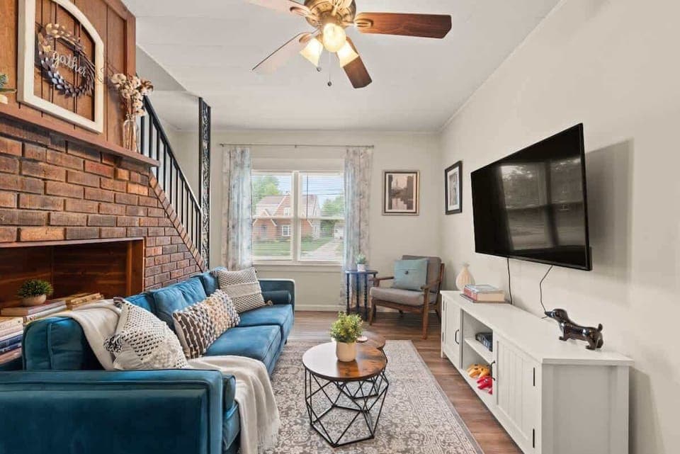 Cozy living room featuring a comfortable blue couch, brick fireplace, a ceiling fan, and a wall-mounted Smart TV. 📺🛋️