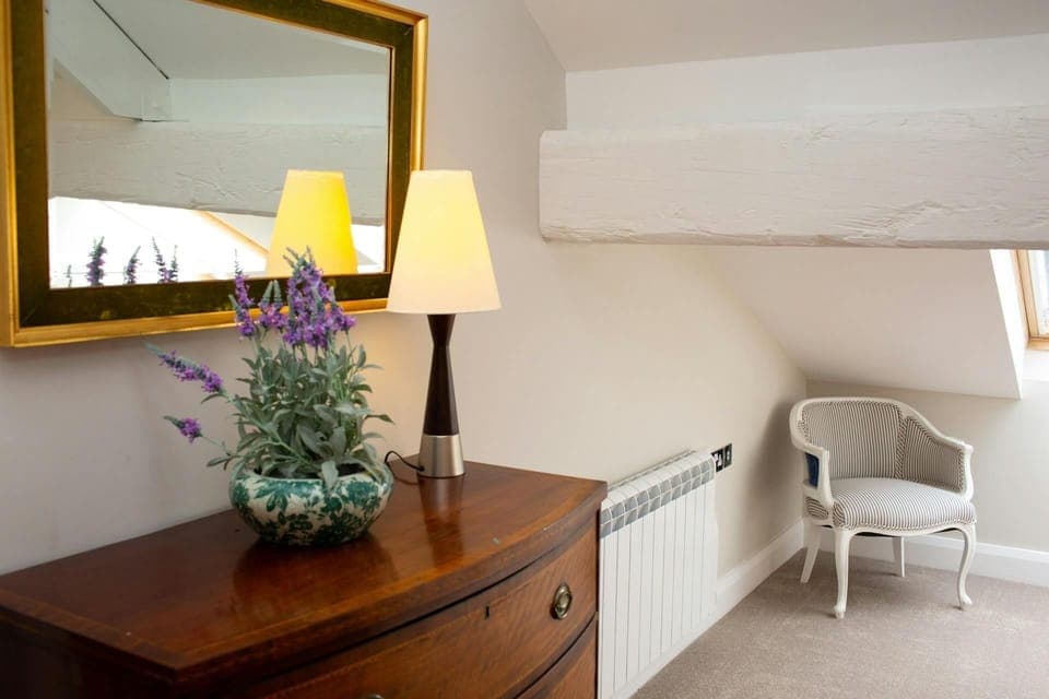 Chest of Drawers with mirror over and a vase of flowers and lamp on top.