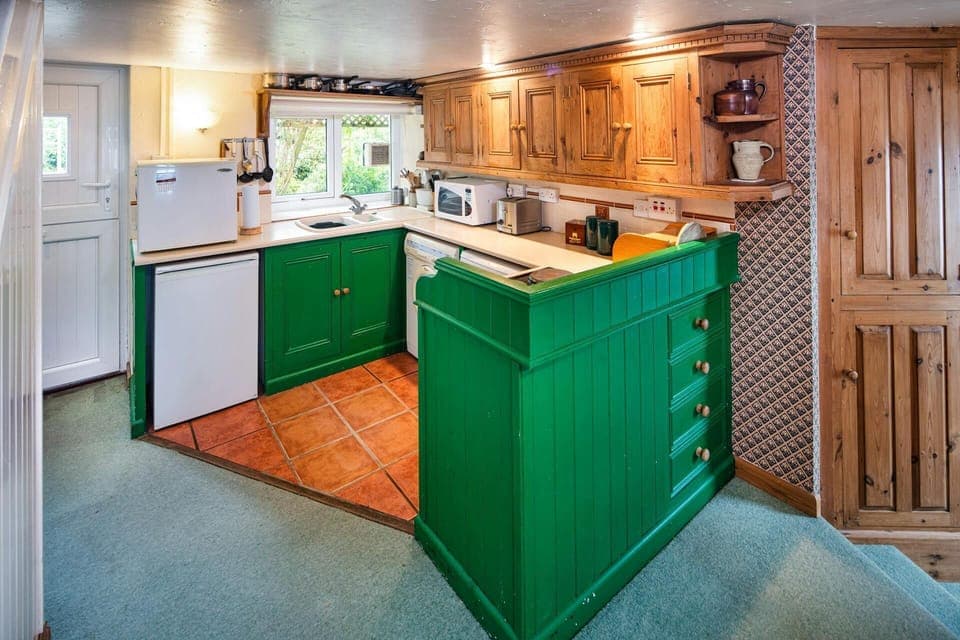 Green base cupboards and pine wall fitted kitchen cupboards: fridge, microwave, toaster and washing machine. Stable door and window looking out to the garden
