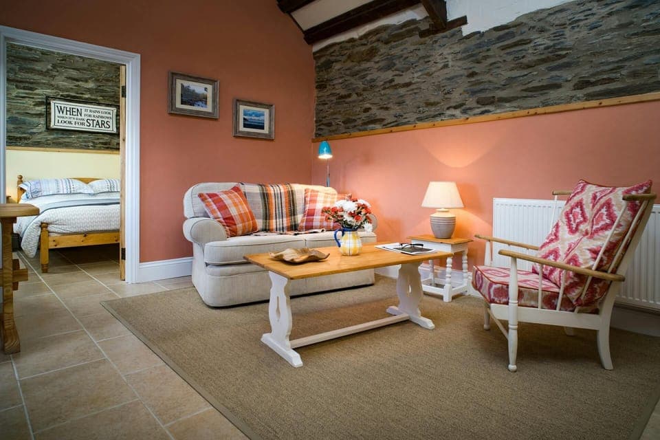 Open plan living area with sofa, chair, coffee table and lamps, doorway leading to bedroom