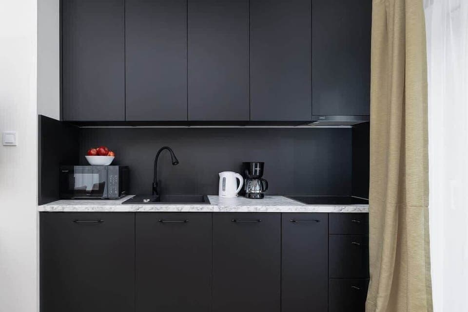 A small, black kitchen with minimalistic equipment. The dark countertops and cabinets give the room a sleek, modern look.