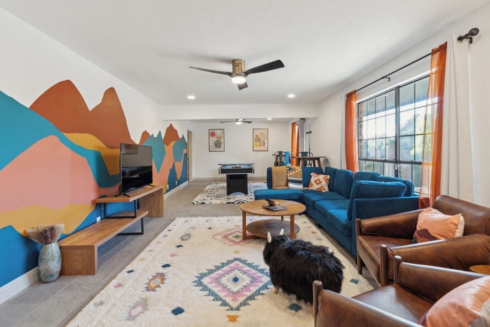 Living room with eclectic couches, ceiling fan, and windows with curtains