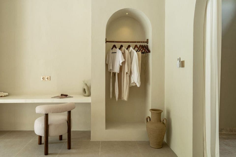 A serene dressing area with arch-inspired robe storage and a simple, stylish workspace.