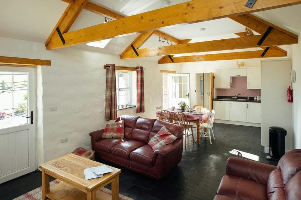 Open plan living room with leather sofas, coffee table, dining table, six chairs and kitchen area