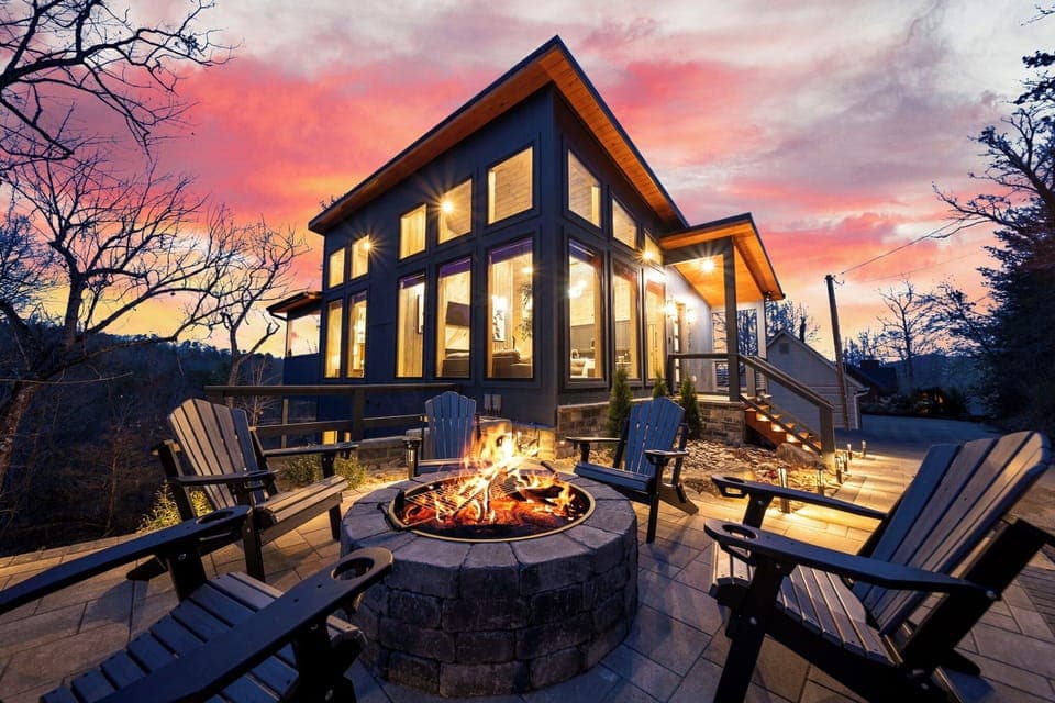 Stunning modern cabin exterior with a glowing fire pit and sunset views.