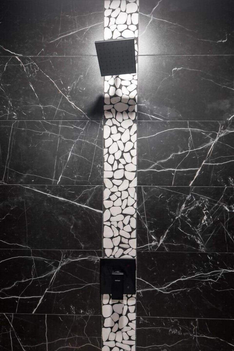 Luxurious black marble shower with pebble accents, rainfall showerhead, and modern design!