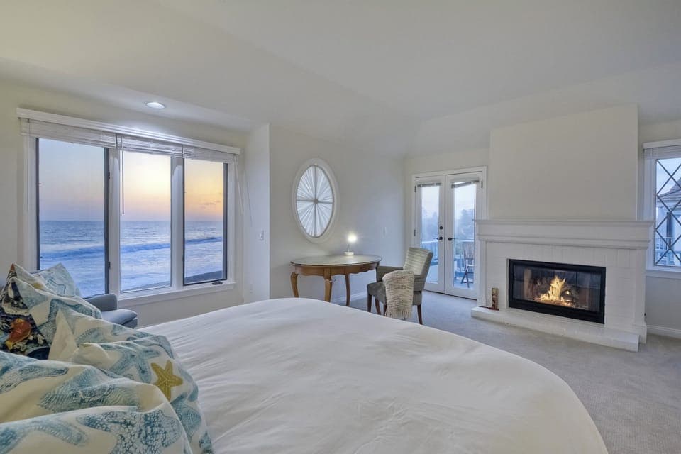 Primary bedroom boasts an ocean view, king-sized bed, gas fireplace and french doors to the oceanfront patio.
