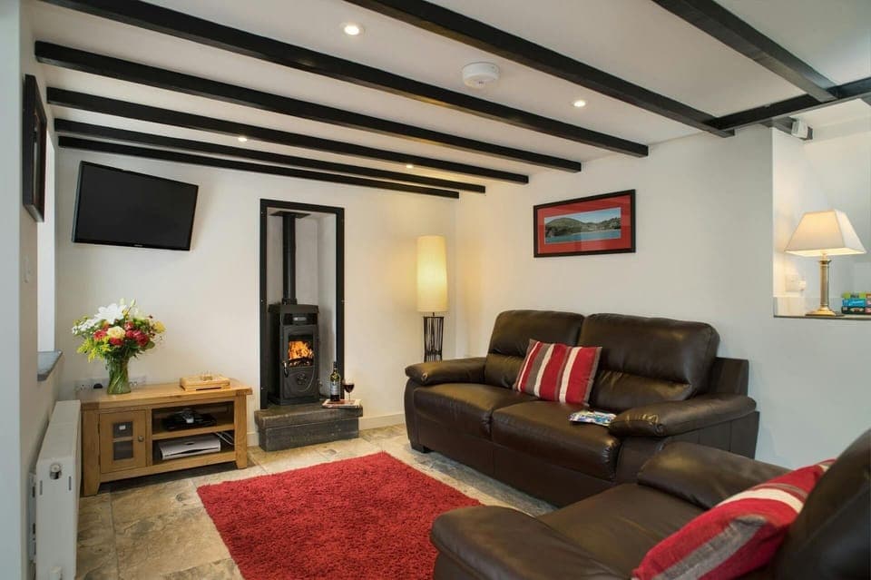 Living area with sofa, armchair, wood burner, lamps, coffee table and wall mounted TV
