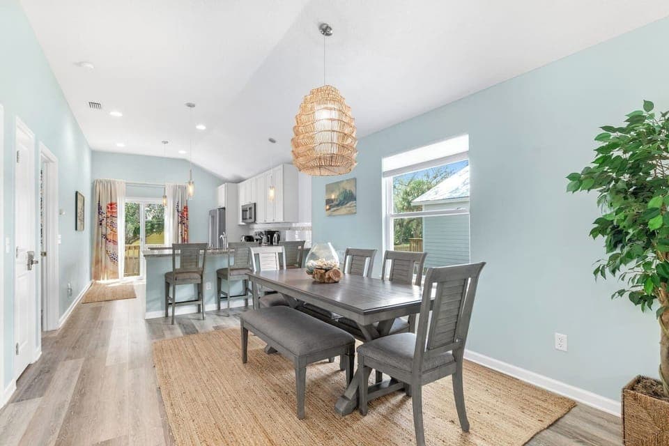Bright and inviting dining area with a spacious table seating 7 guests, complemented by 3 stylish bar stools for extra seating.