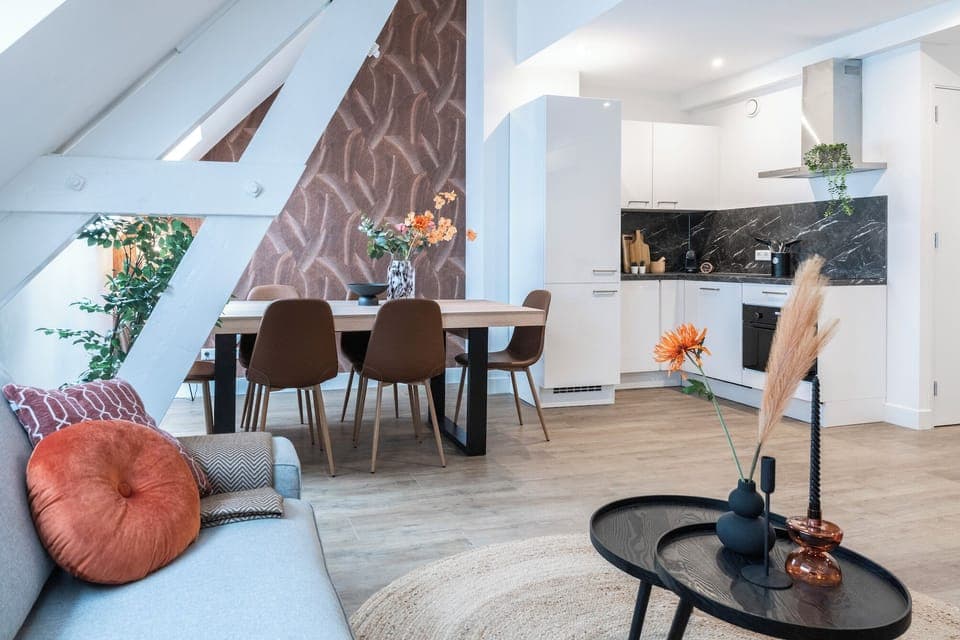 A stylish open living space with a modern dining area, cozy sofa, and a well-equipped kitchen, complemented by vibrant décor.