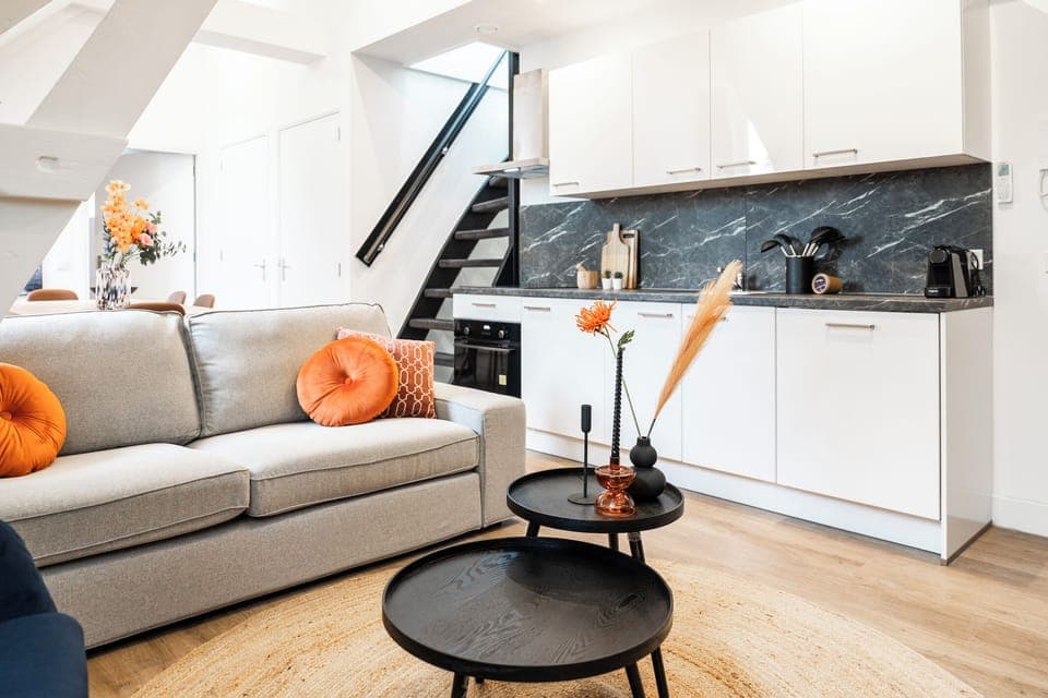 A bright living area with a modern sofa, stylish décor, and a well-equipped kitchen corner, creating a functional and inviting atmosphere.