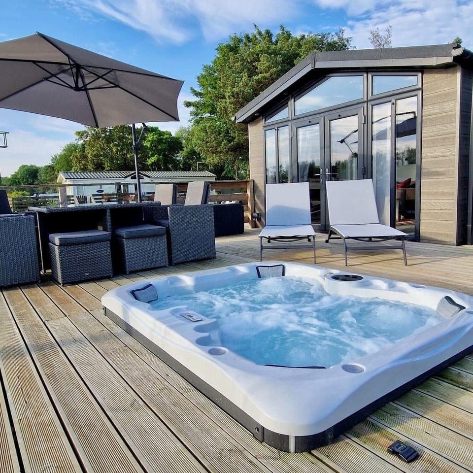 The lodge boasts a spacious wooden deck at the rear, complete with a four-person outdoor dining table, parasol, sun loungers and a hot tub. This inviting area offers stunning views of the lake