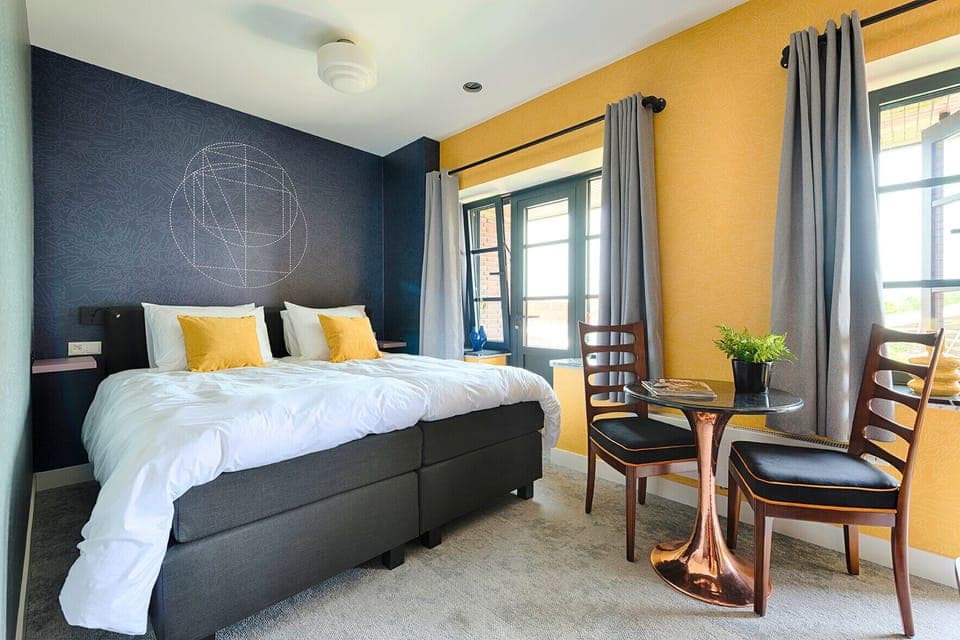 Stylish Tilburg bedroom with twin beds pushed together for extra comfort, warm accent colors, and natural light from the large windows