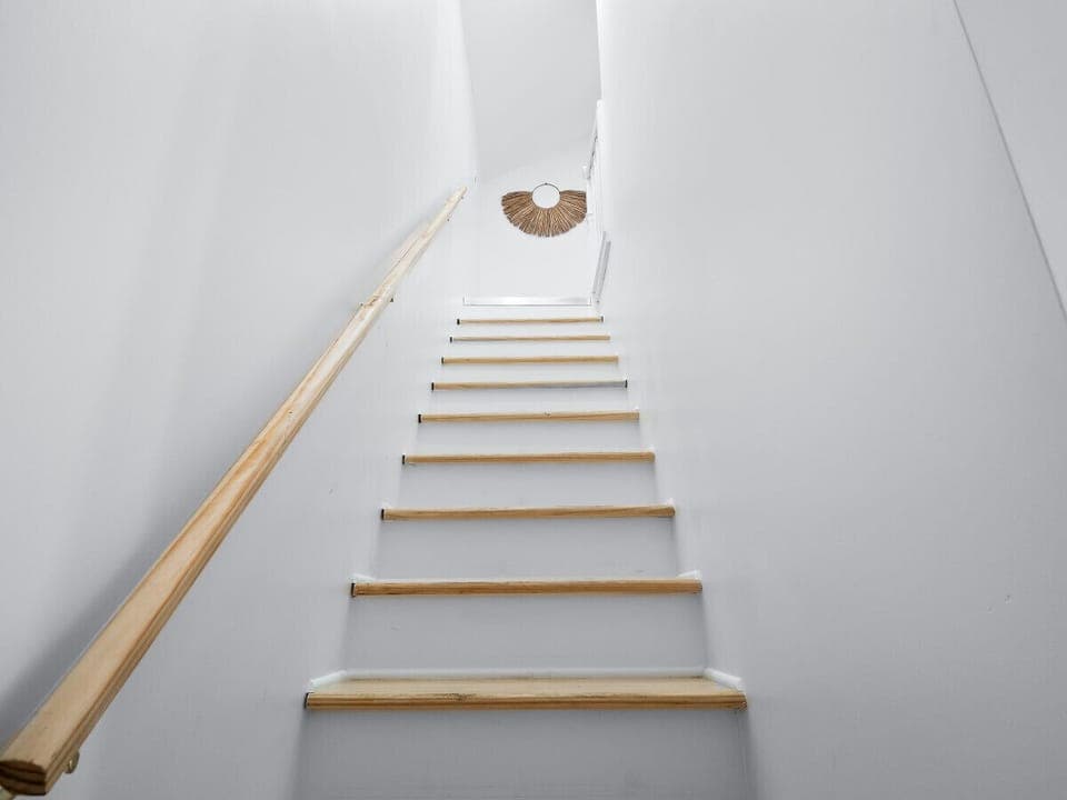 Bright staircase with light wood steps and simple design   - Minimal Airbnb style with warm natural light above   - Leading guests to private upper-level bedrooms