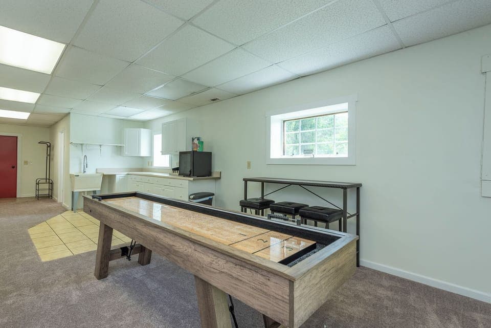 Lower-level game room with an arcade game, shuffleboard table, sectional seating, and 65" Smart TV