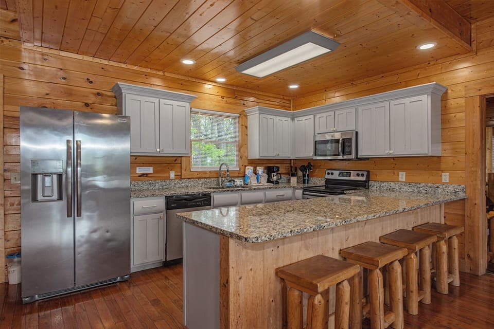 Your fully equipped kitchen features granite countertops, stainless steel appliances, and rustic log stools perfect for casual meals.