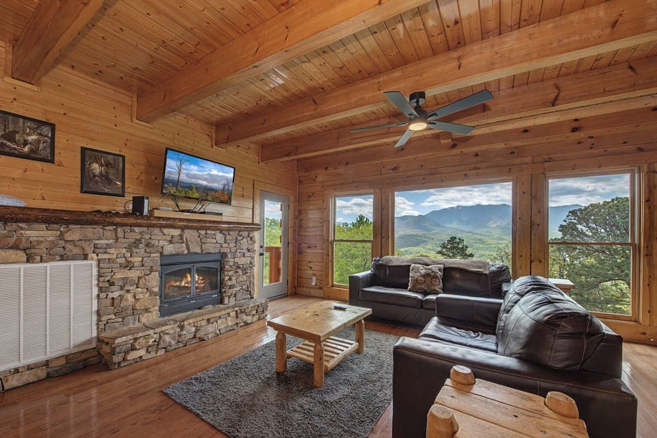 Relax in this cozy mountain cabin living room with panoramic views, stone fireplace, and rustic charm perfect for your getaway.