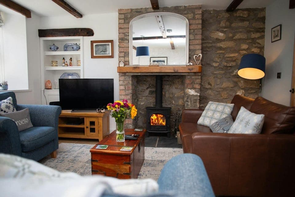 Lounge with TV, wood burner and mirror above on stone featured wall