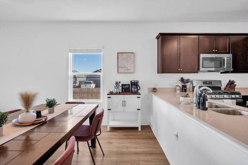 Bright and modern kitchen and dining area featuring a large wooden table with stylish seating for six. The kitchen is fully equipped with stainless steel appliances, a coffee station, and ample counter space—perfect for cooking and gathering.