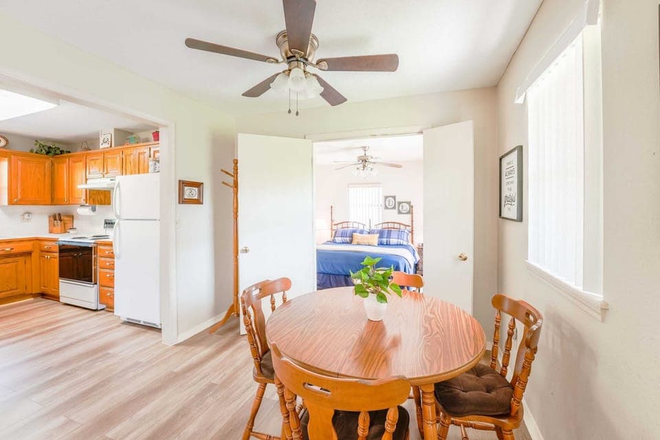 Bright and cozy dining area with a view into the kitchen and bedroom, featuring warm wooden furniture and natural lighting.