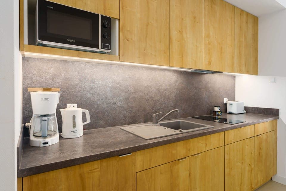 A modern kitchenette with wooden cabinets, equipped with a coffee machine and kettle on the countertop.