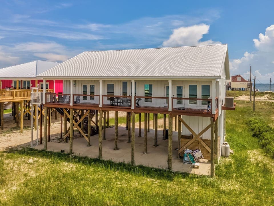 Elevated coastal home on stilts with wraparound deck and natural dune surroundings in beachfront community.