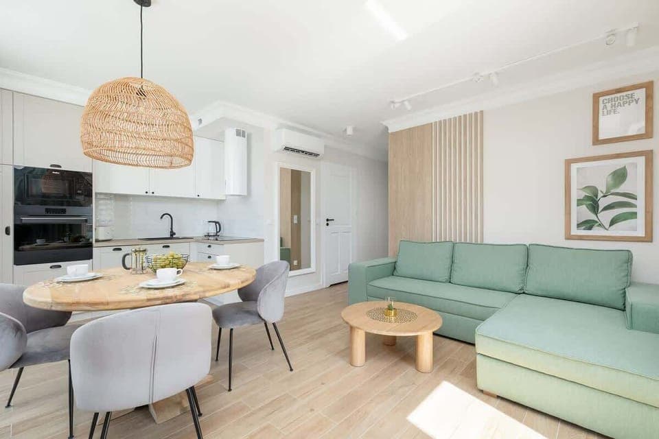 A bright and modern living room with a mint green sectional sofa, a wooden coffee table, and a dining area in the background featuring a round table with elegant chairs.