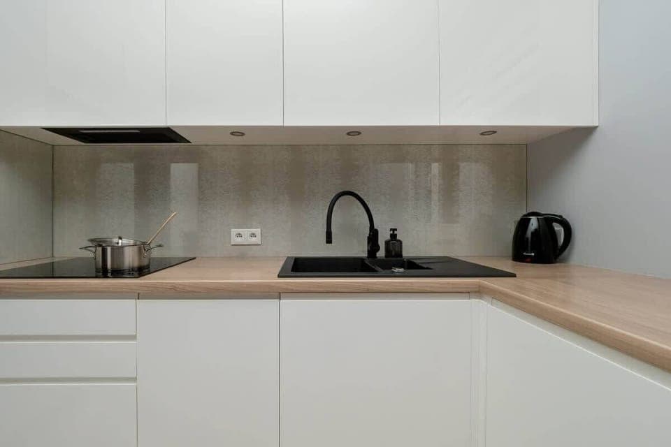Modern white kitchen with light wood countertop and black sink.
