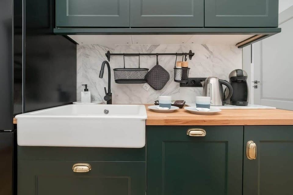 Modern kitchen with dark green cabinets, a farmhouse sink, and wooden countertops, creating a warm and elegant look.