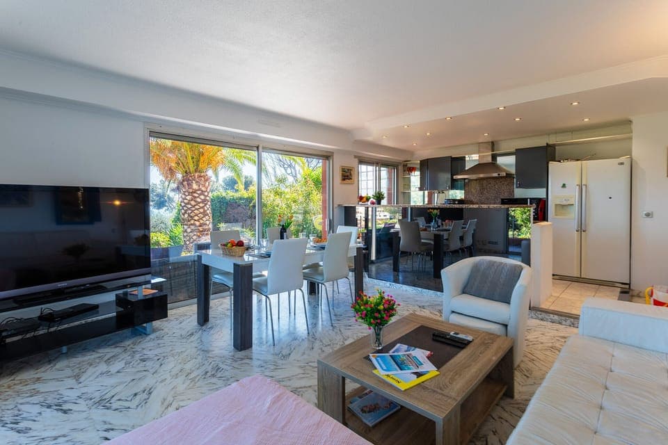 Bright living room with garden view, modern furniture, dining area, and a well-equipped open kitchen.