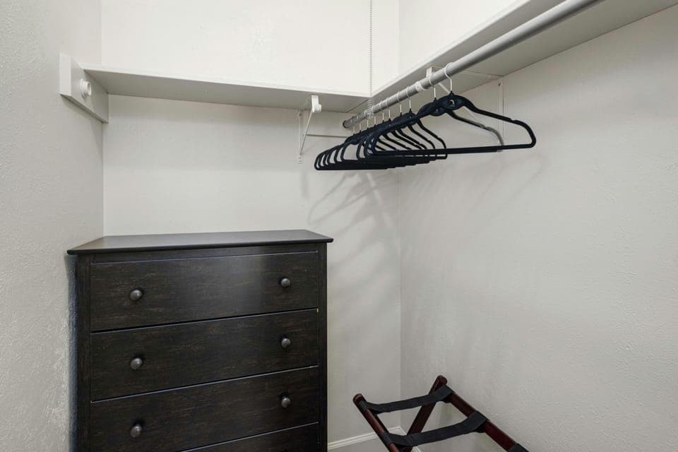 The second bedroom features a spacious walk-in closet equipped with a dresser, hangers, laundry hamper, and a convenient luggage rack for optimal storage and organization.