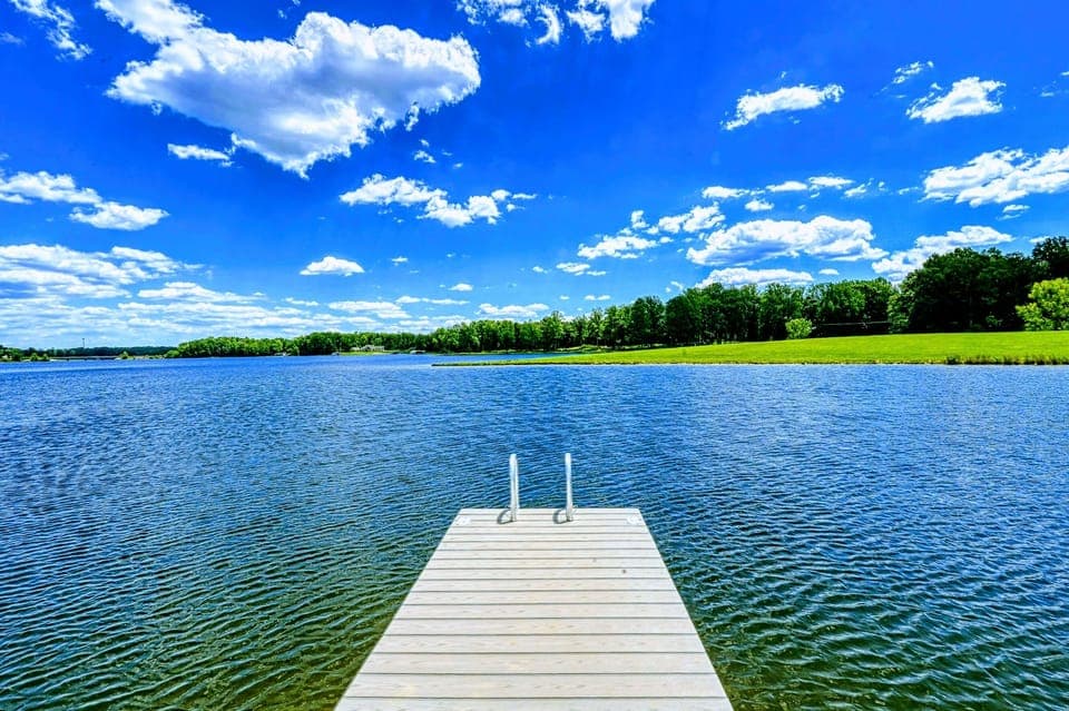 Picturesque dock extending into a clear, tranquil lake under a vibrant blue sky, perfect for a refreshing swim or peaceful retreat