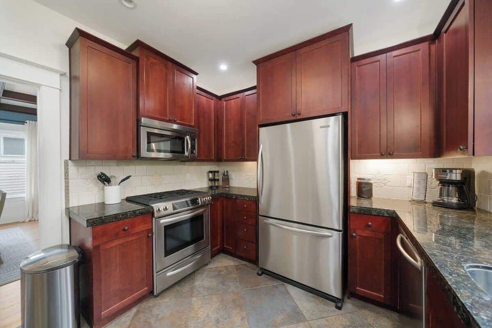 Fully equipped kitchen with stainless steel gas stove, ample prep space, and large refrigerator.