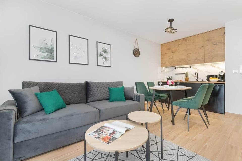 A stylish living room featuring a gray sofa, round dining table, and soft wall decor. The room is bright and welcoming with modern furnishings.
