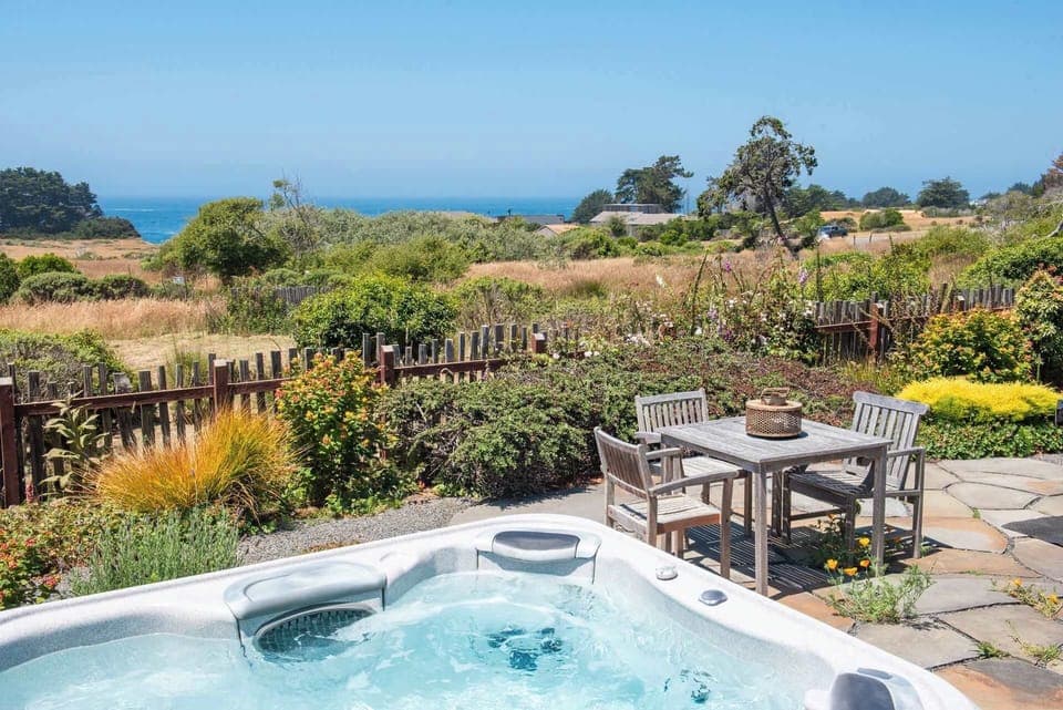 Bask in the serene backyard retreat with a hot tub and distant ocean views under a clear blue sky