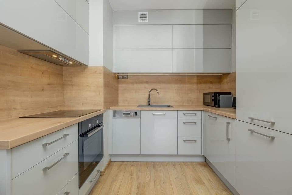 Contemporary kitchen with white cabinets, wooden backsplash, and built-in appliances.